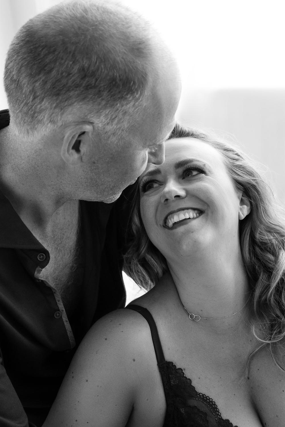 Black and white intimate portrait of a smiling woman looking up at a man who leans in close to her face.