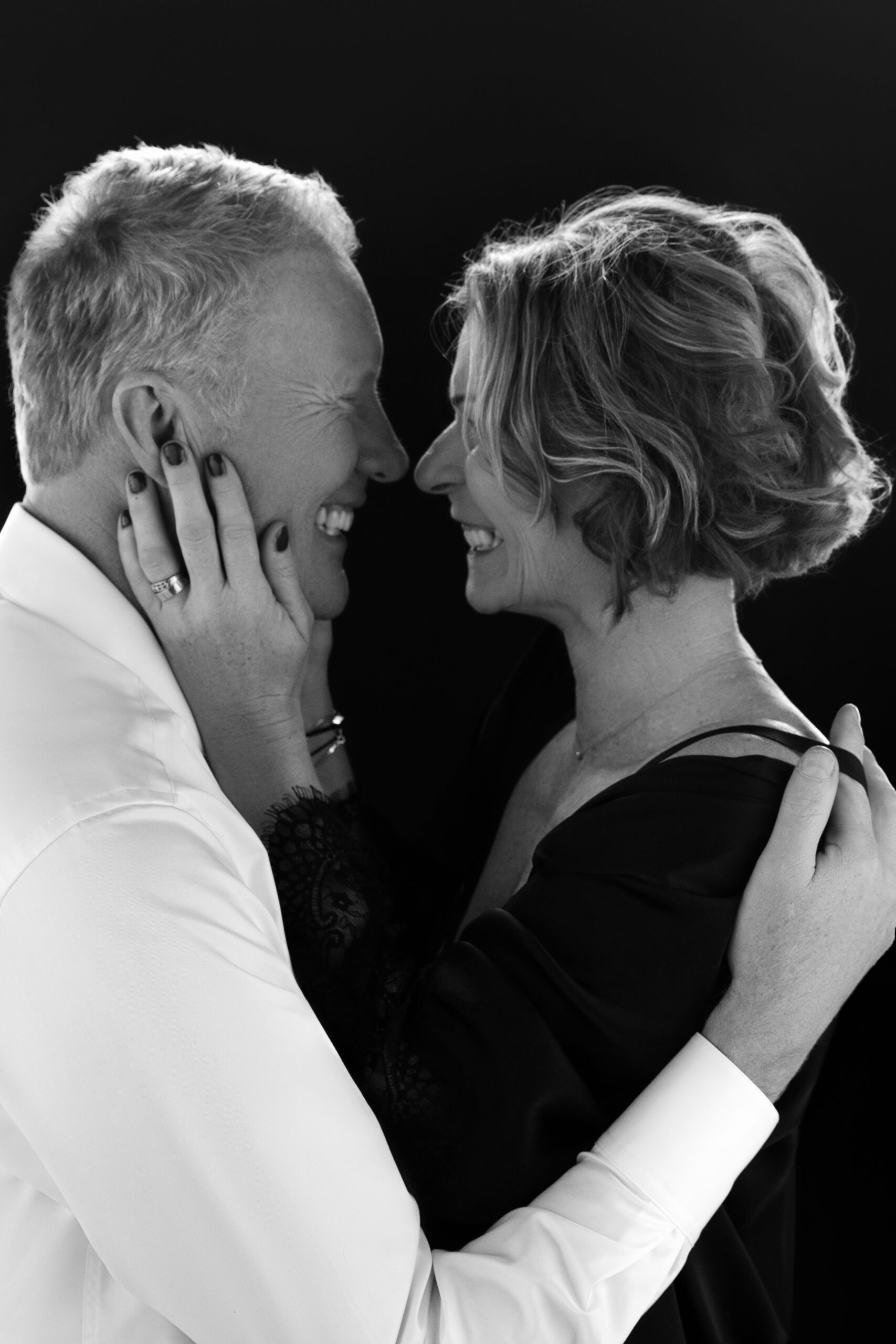 Black and white portrait of a smiling couple facing each other, embracing closely with the woman gently holding the man's face.