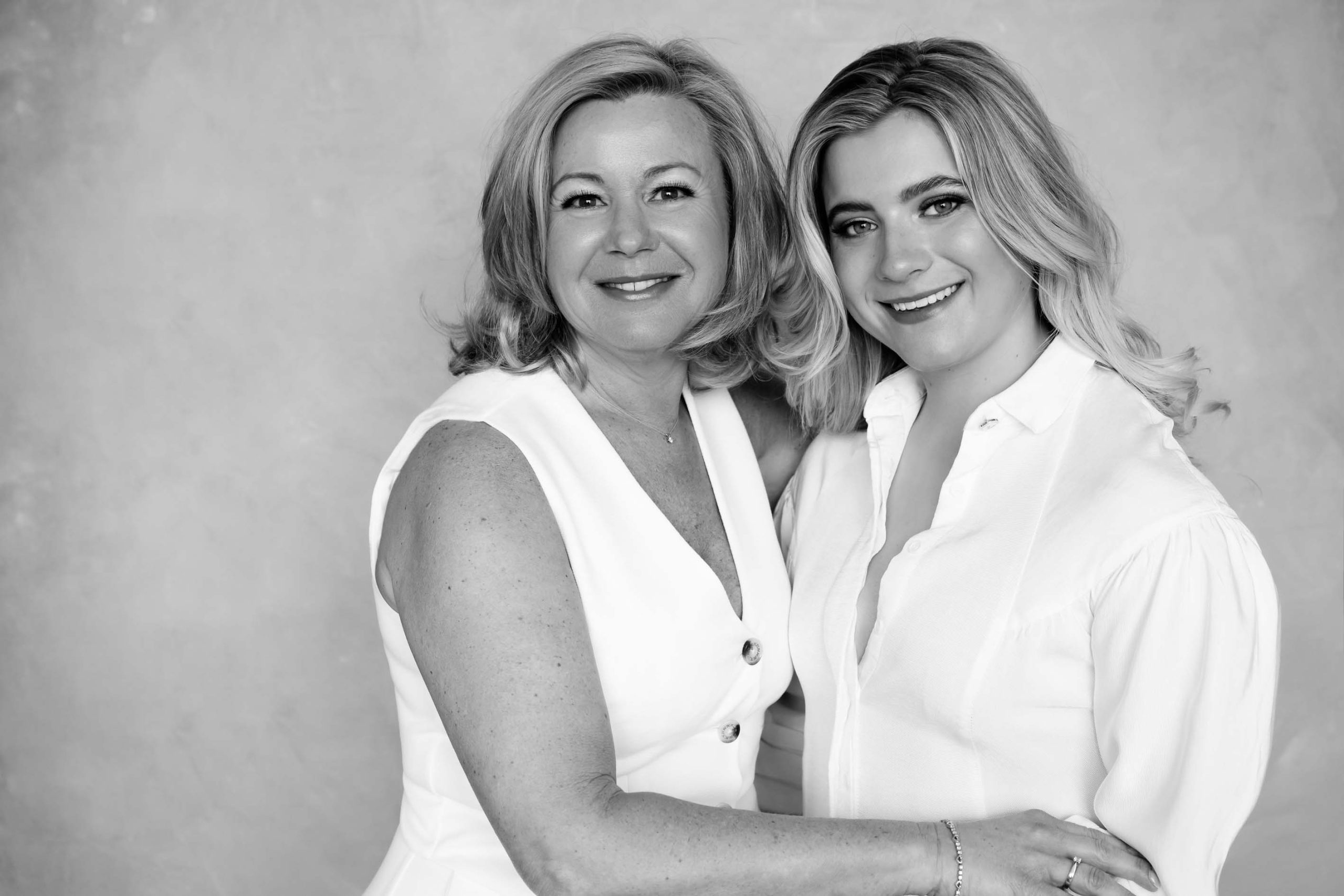 Black and white portrait of two smiling women, one older and one younger, embracing each other against a plain background.