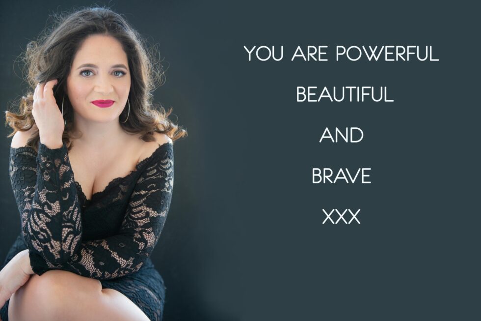 A woman with shoulder-length curly hair wearing a black lace off-the-shoulder dress sits against a dark background, touching her hair and smiling slightly. To her right, text reads: YOU ARE POWERFUL BEAUTIFUL AND BRAVE XXX.