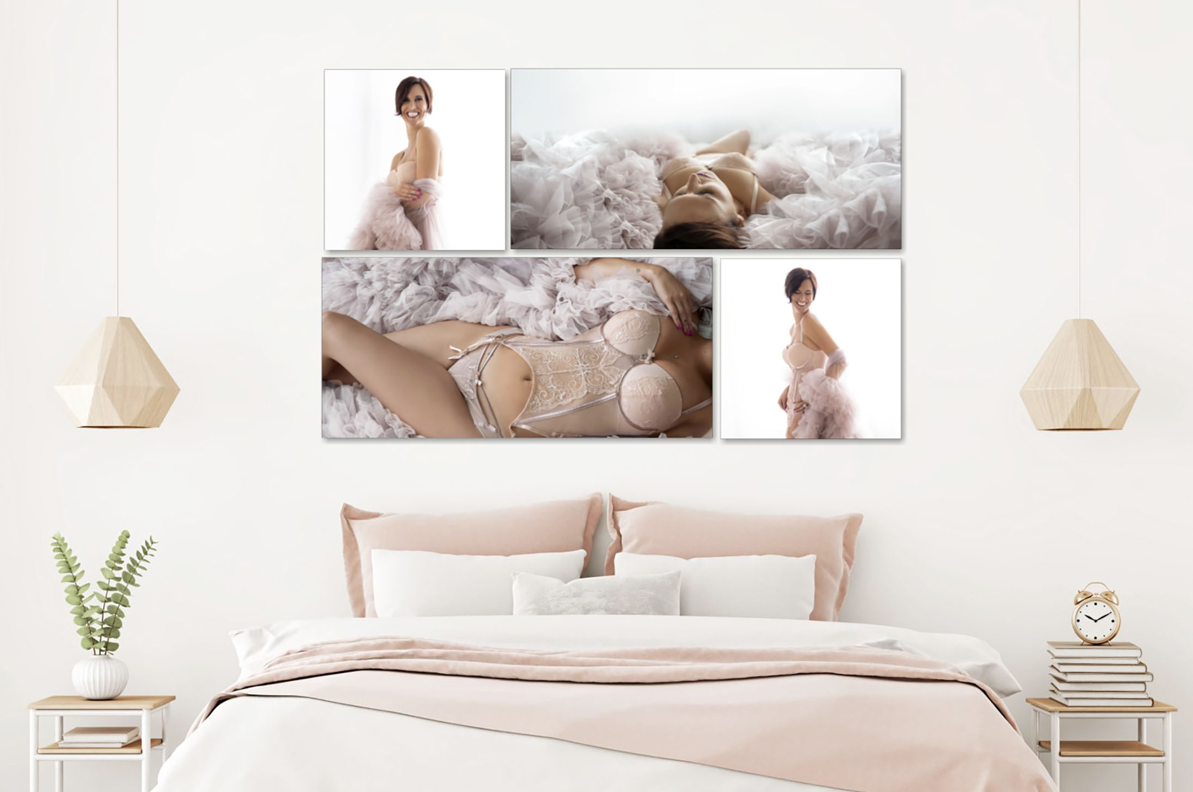 A modern bedroom with a white and blush pink color scheme featuring a large bed with multiple pillows and a blush pink blanket, two wooden geometric pendant lights hanging from the ceiling, and two side tables with a plant on the left and an alarm clock on a stack of books on the right. Above the bed, five framed boudoir photographs of a smiling woman in light pink lingerie and a fluffy pink wrap are displayed in a grid arrangement on the wall.